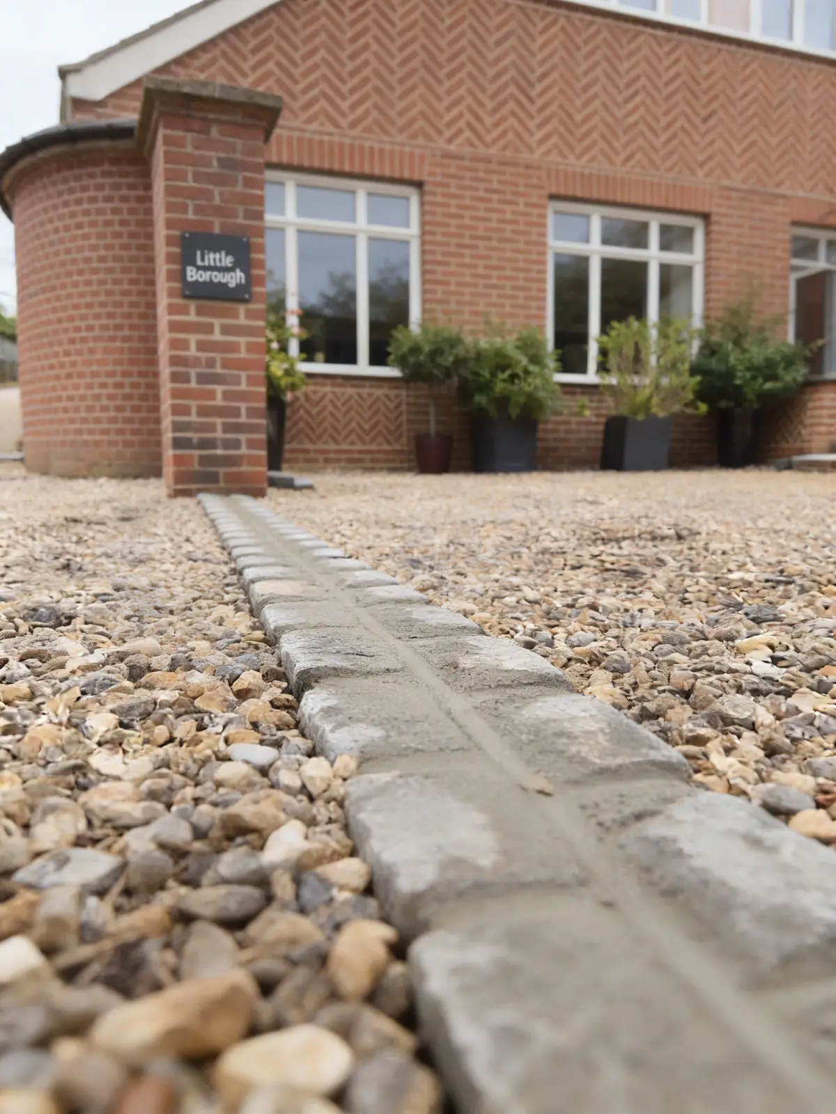 Gravel driveway with a natural stone sett drainage channel leading to a brick house
