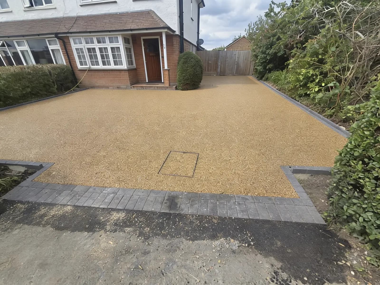 Finished gold resin-bound driveway with a charcoal block-paving border outside a Surrey home